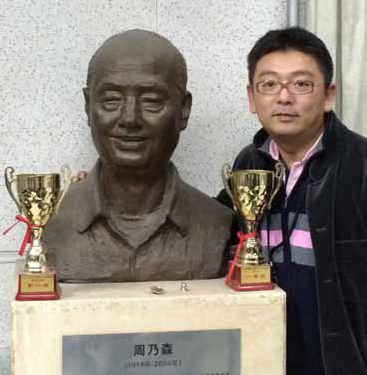 Cellist Yao Zhao poses with a statue of his grandfather before a San Diego Symphony concert at Tsinghua University in Beijing, China. The statue was erected upon the grandfather’s death to honor his long years service as the university’s band director. The grandfather is the one with the bigger smile.